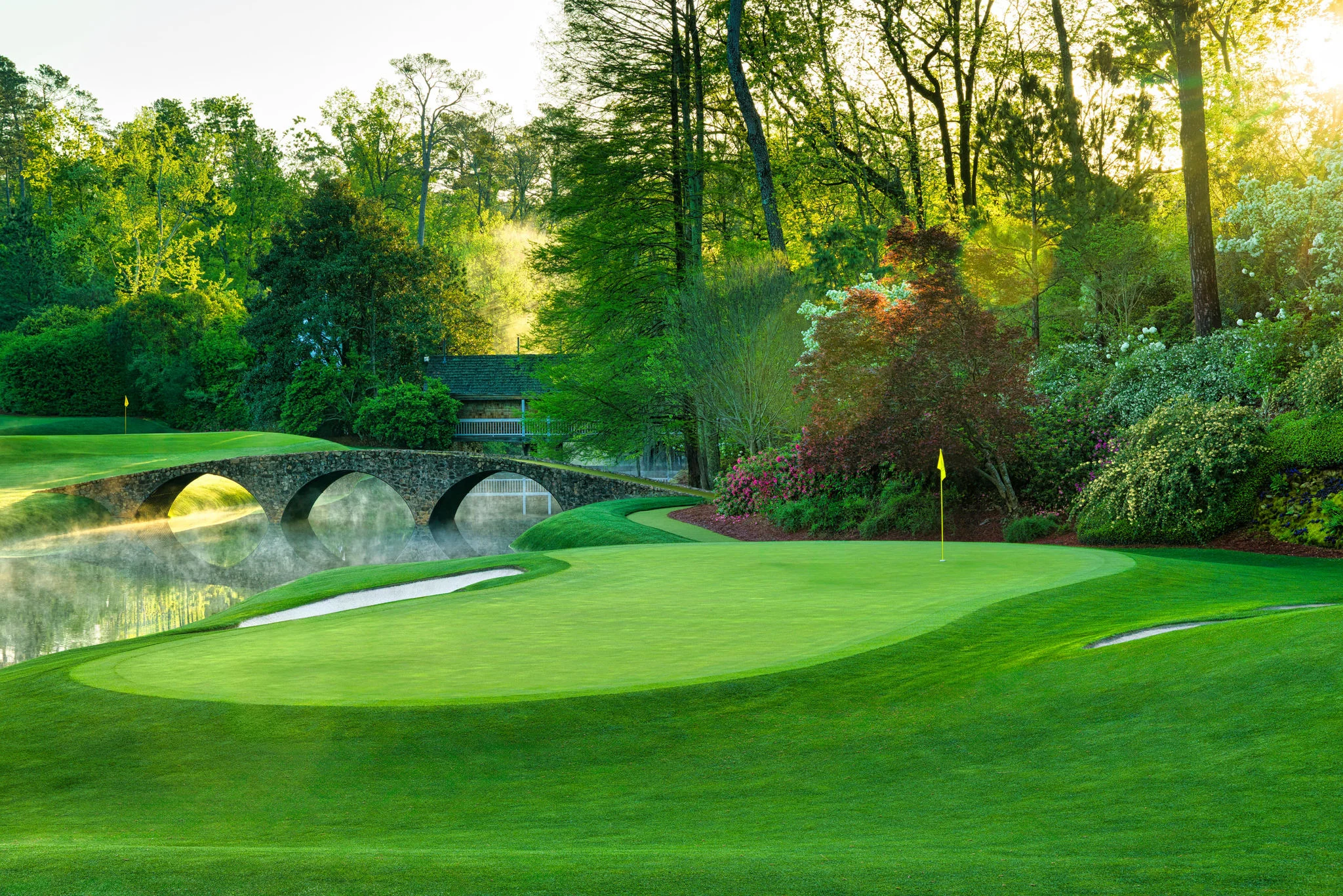 Sunlit golf course with stone bridge and lush greenery